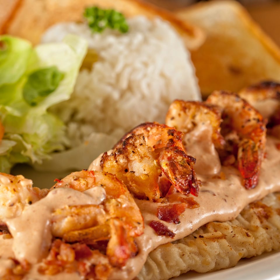 Grilled shrimp and chicken drizzled with creamy sauce, served alongside rice, lettuce, tomato, and onion.