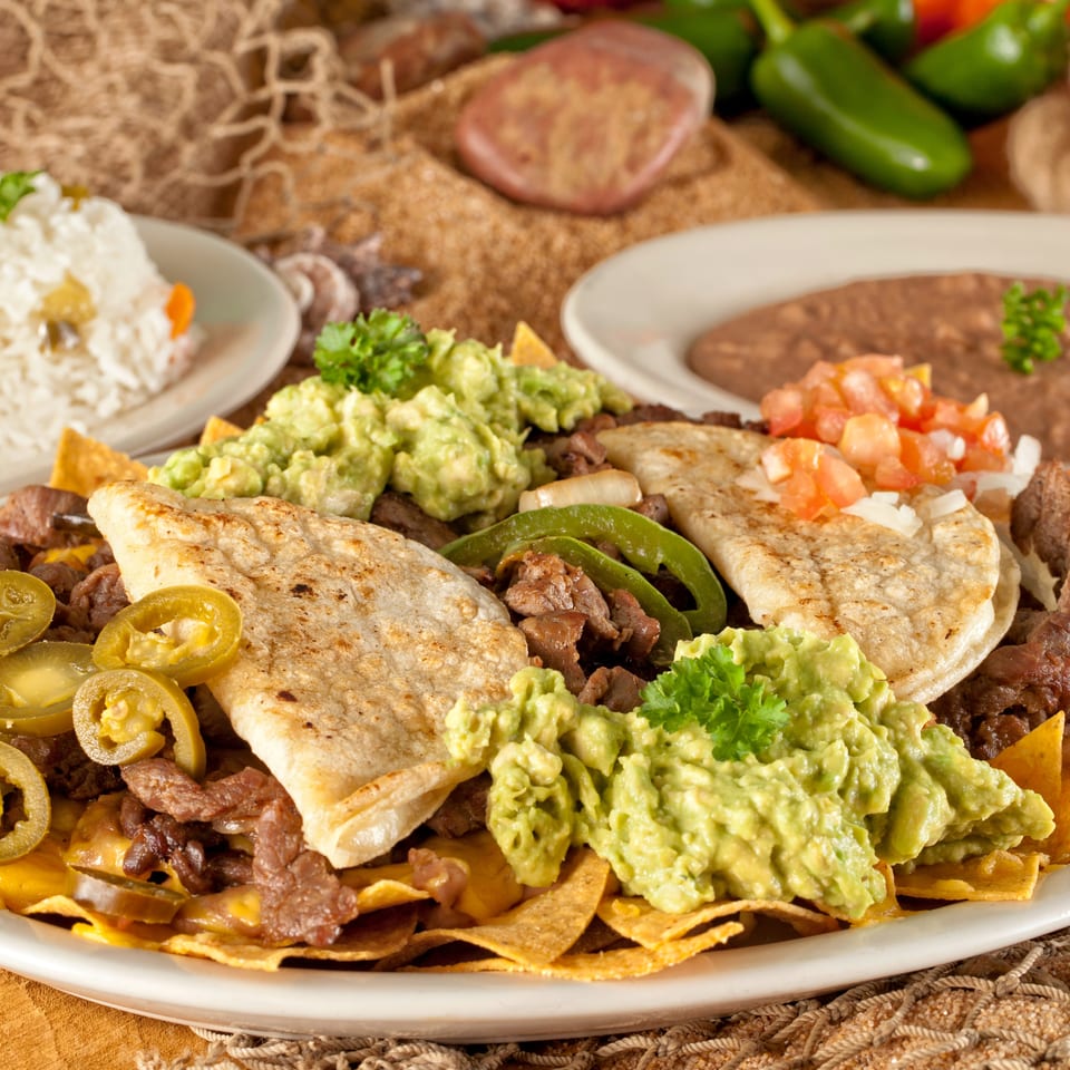 Loaded nachos topped with steak, guacamole, jalapeños, quesadillas, pico de gallo, and rice with refried beans.